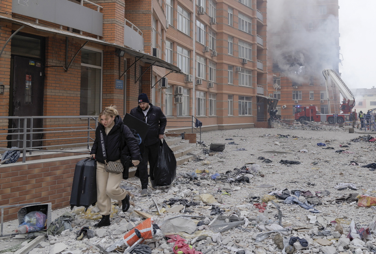 Foto de um homem e uma mulher com malas em uma cidade devastada da Ucrânia