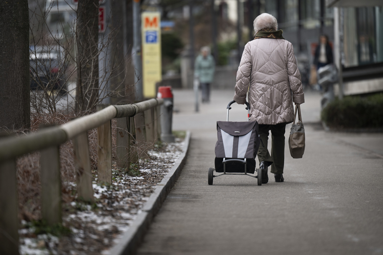 Alte Frau läuft mit Einkaufswagen auf einem Trottoir