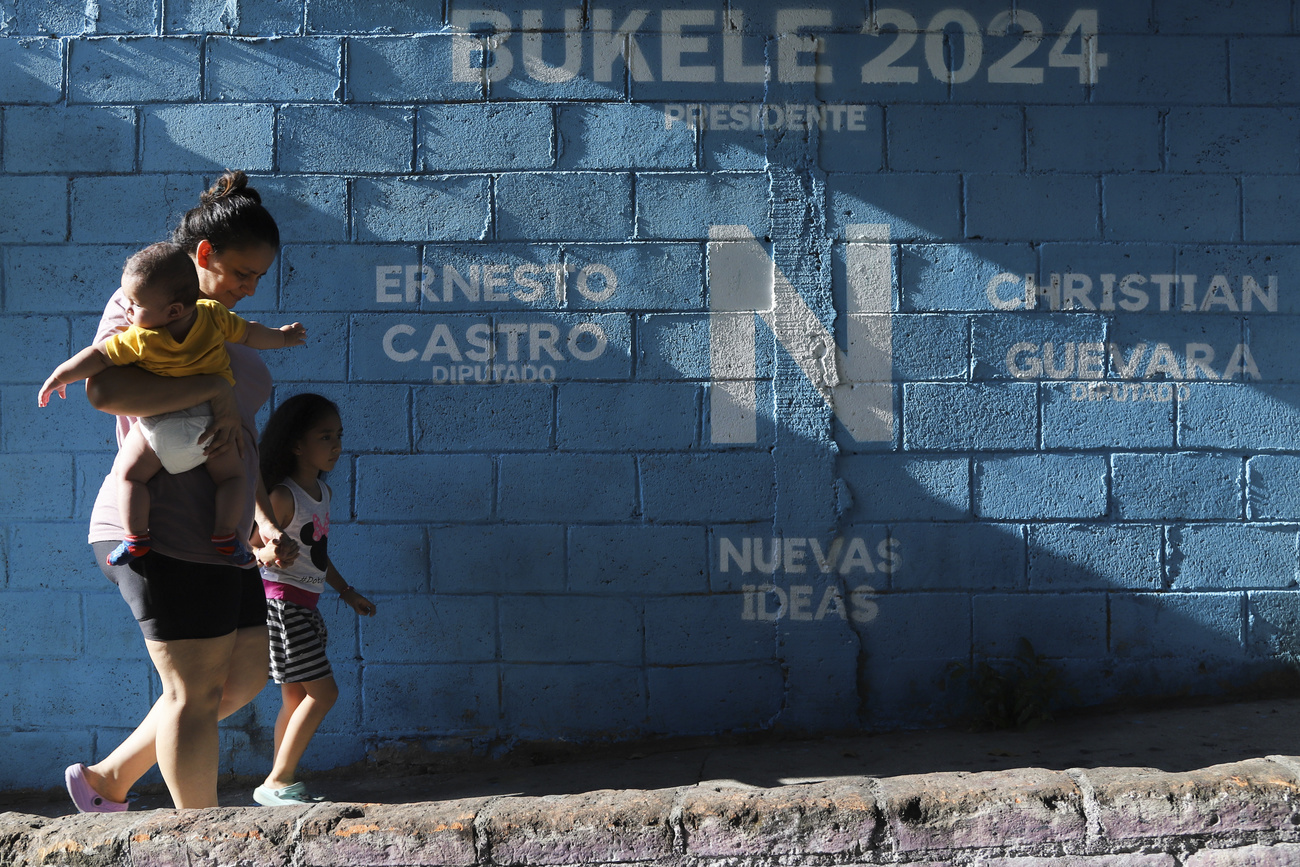 Eine Frau mit zwei Kinder in El Salvador läuft an Wahlwerbung für Bukele vorbei.