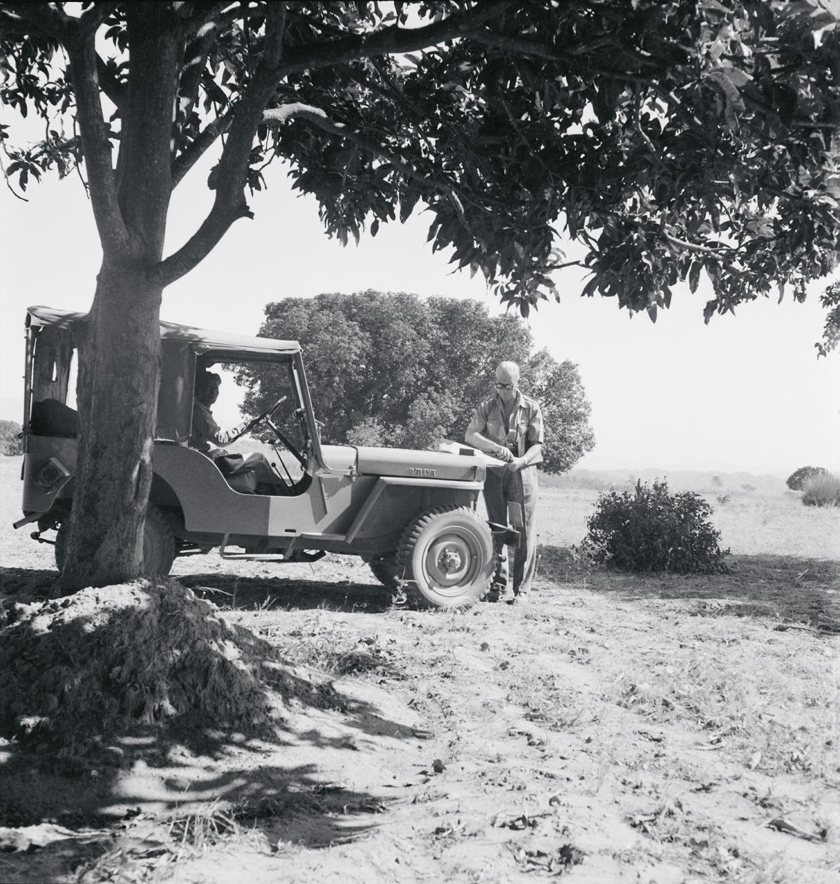 un uomo esamina una mappa appoggiata sul cofano di jeep in una foto in bianco e nero