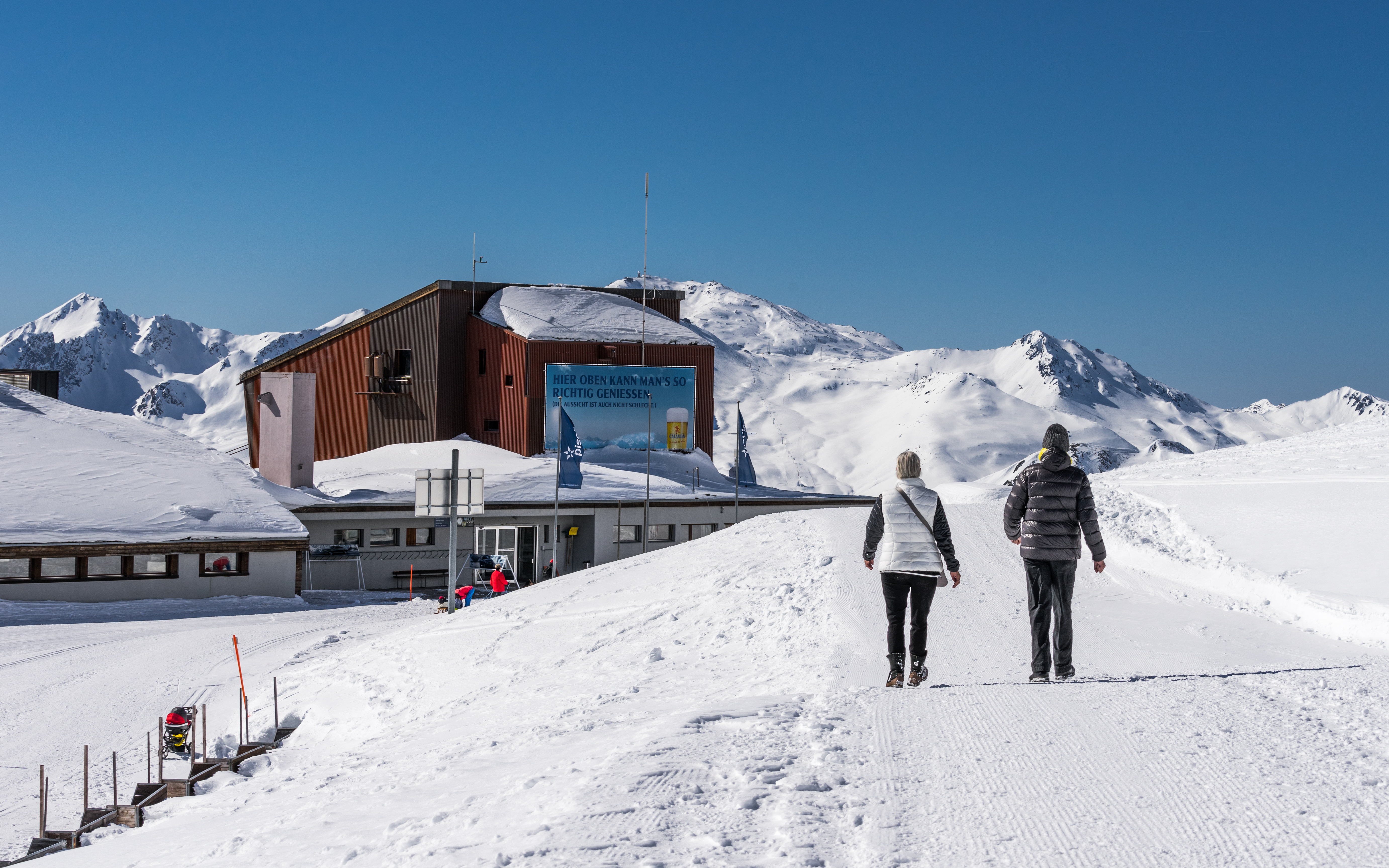 雪道を歩く男性と女性の後ろ姿と山小屋