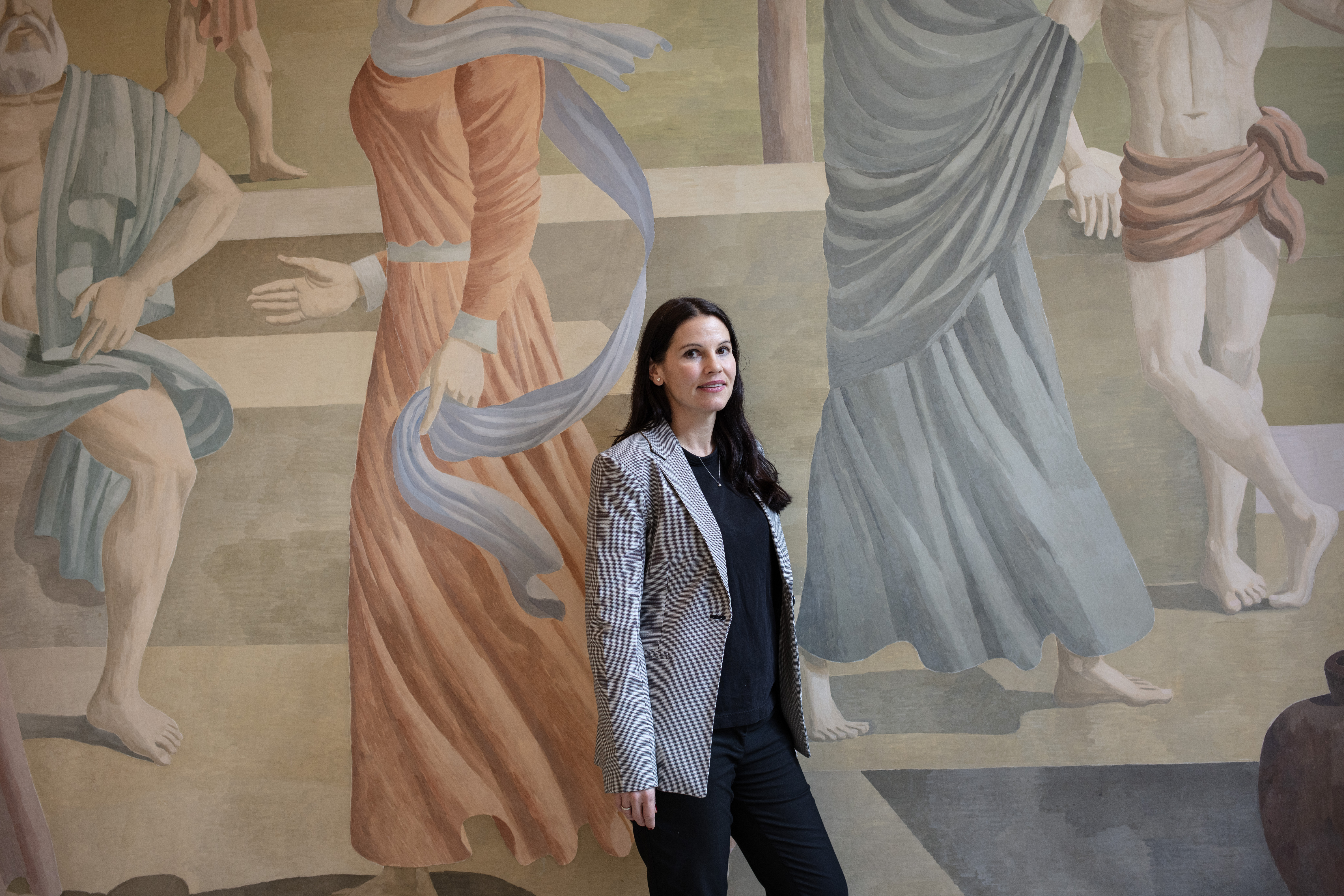 woman pictured in front of large classical mural