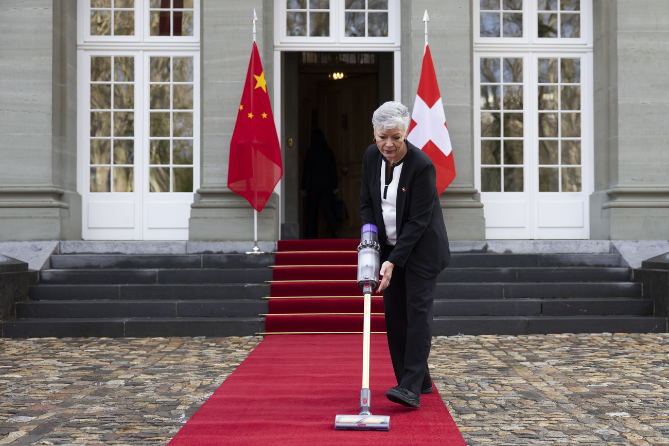 Person vacuums red carpet next to Chinese and Swiss flags