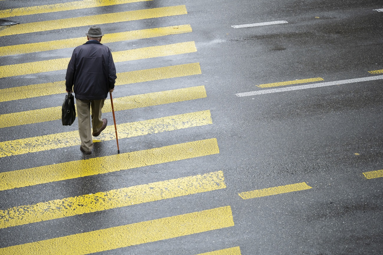 old man walking across the street with a cane