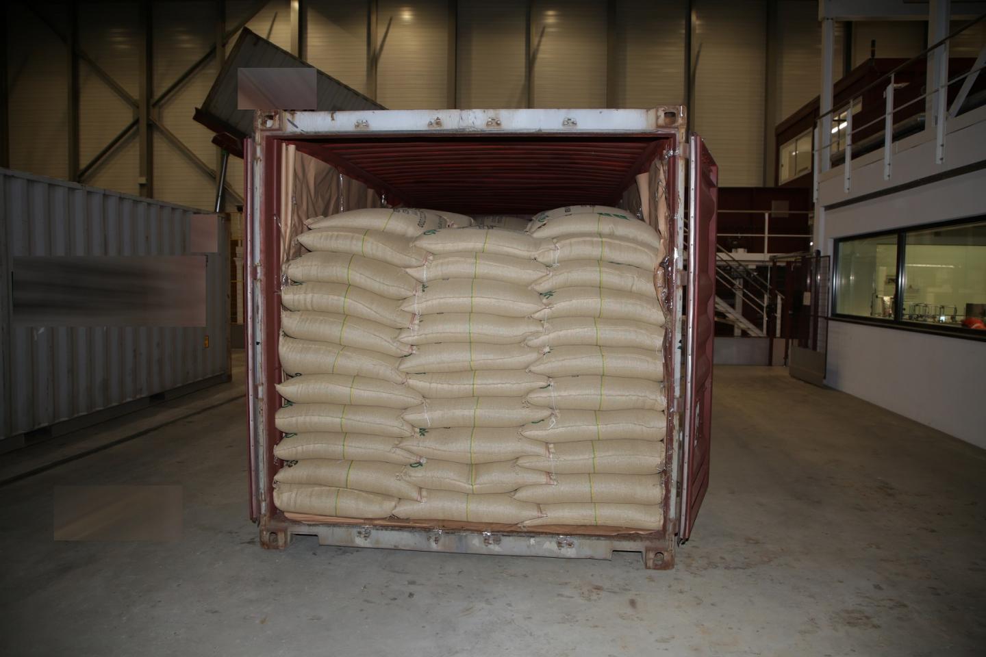 Ein offener Container, gefüllt mit Jutesäcken in einer Lagerhalle.