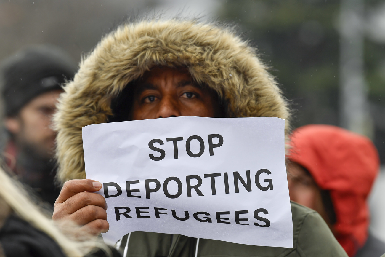 رجل يرفع لافتة "أوقفوا ترحيل اللاجئين واللاجئات
