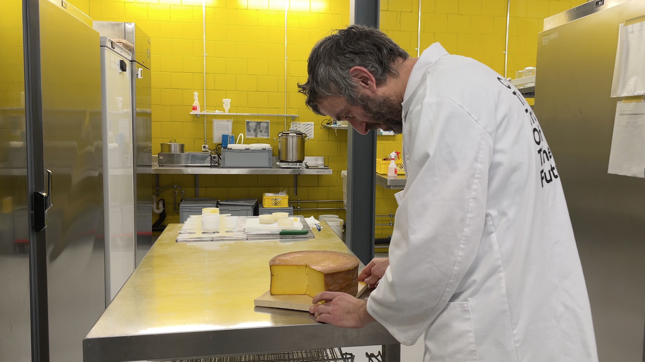 A man looking at a vegan cheese wheel on a table.