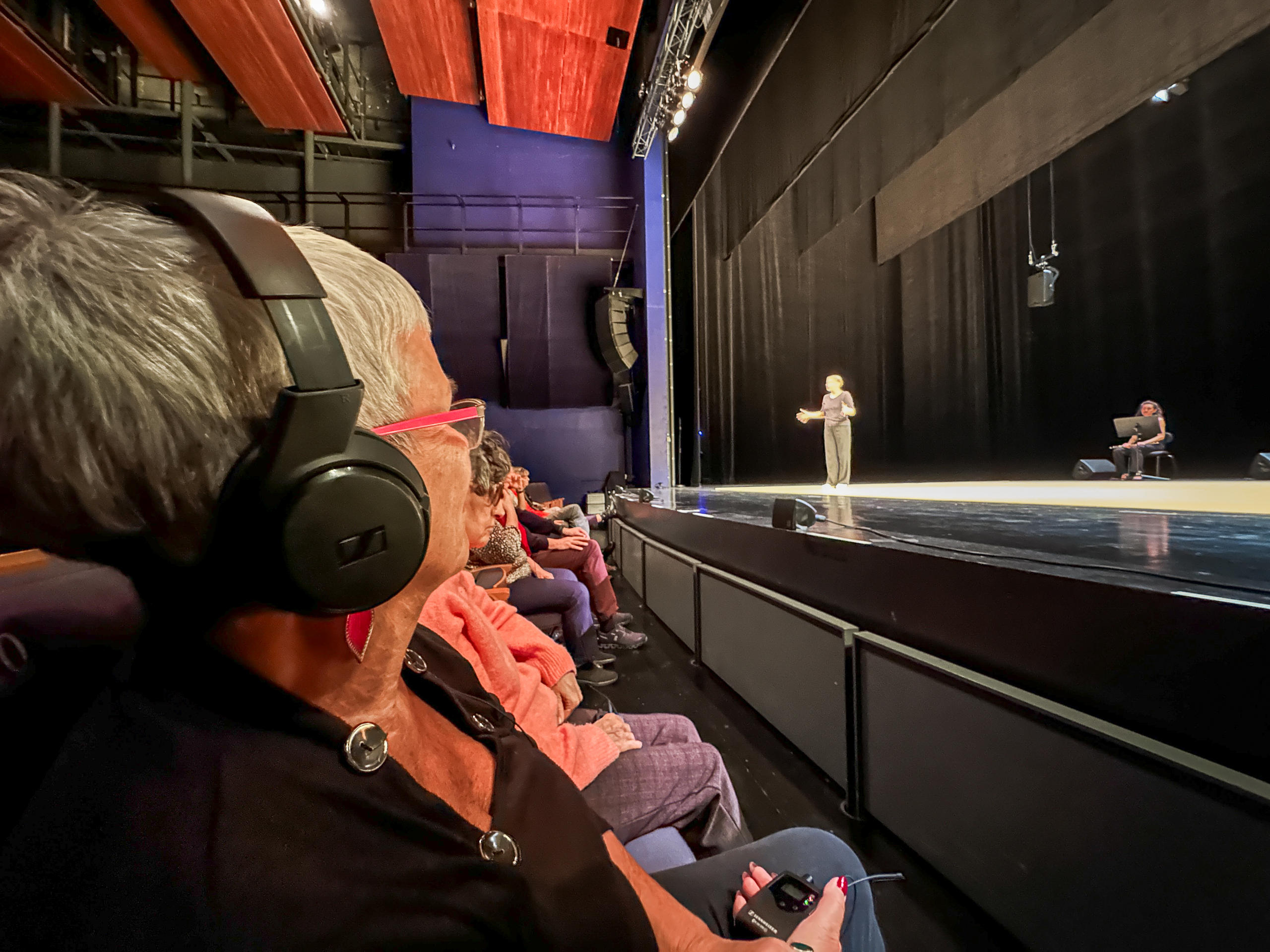 Frau mit Kopfhörer, die in der ersten Reihe eines Theatersaals sitzt