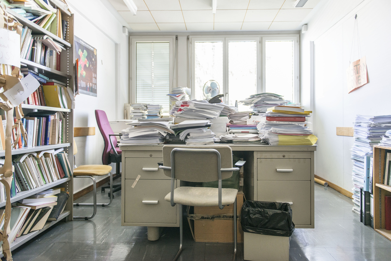 Bright office with lots of light and stacks of paper on a desk that is in the middle of the room.