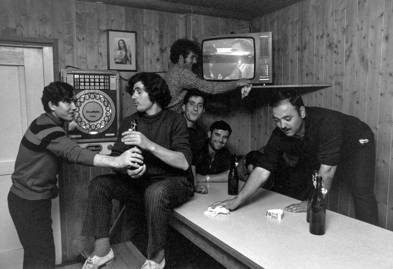 Lavoratori stagionali italiani bevono birra nel tempo libero nel soggiorno della loro baracca e guardano la televisione ad Adliswil, nel canton Zurigo, nel 1972.