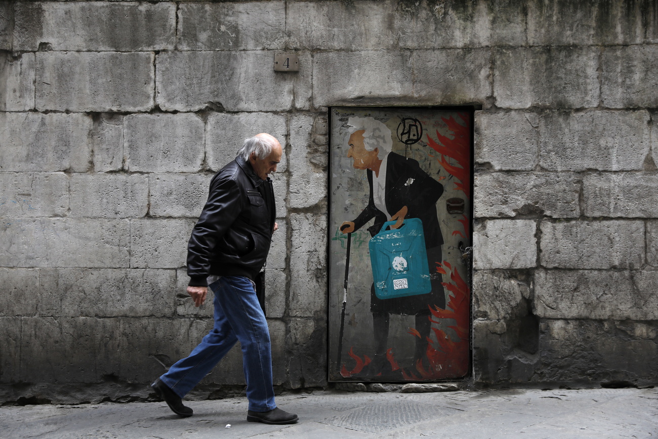 Un anziano vicino a un graffito che ritrae una persona anziana nel centro a Siena.