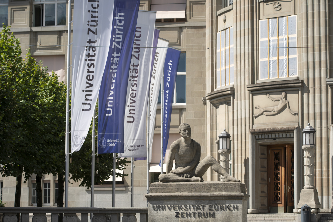 Old Zurich university building with blue and white flags and a statue