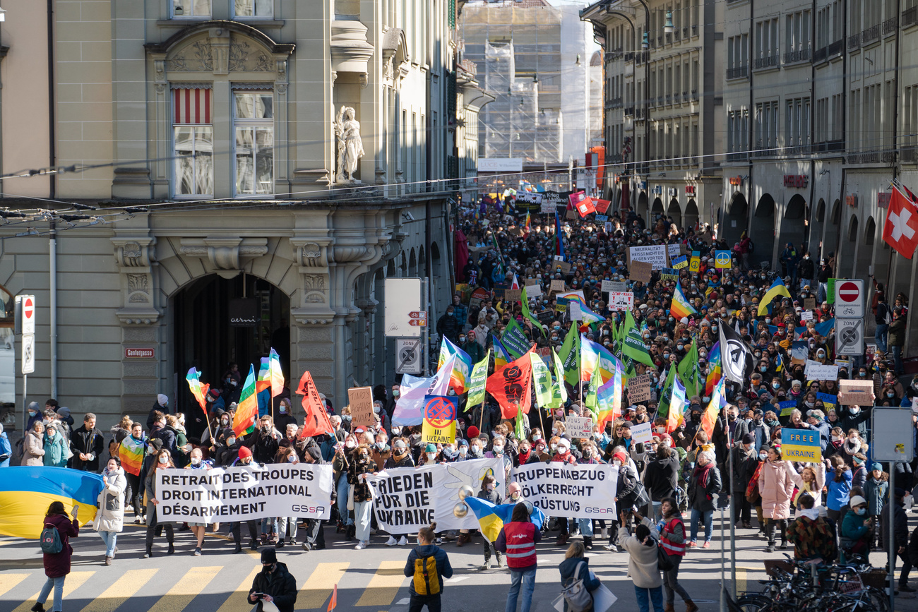 A large gathering of people with banners and flags march through the city of Bern. Birds-eye view point.