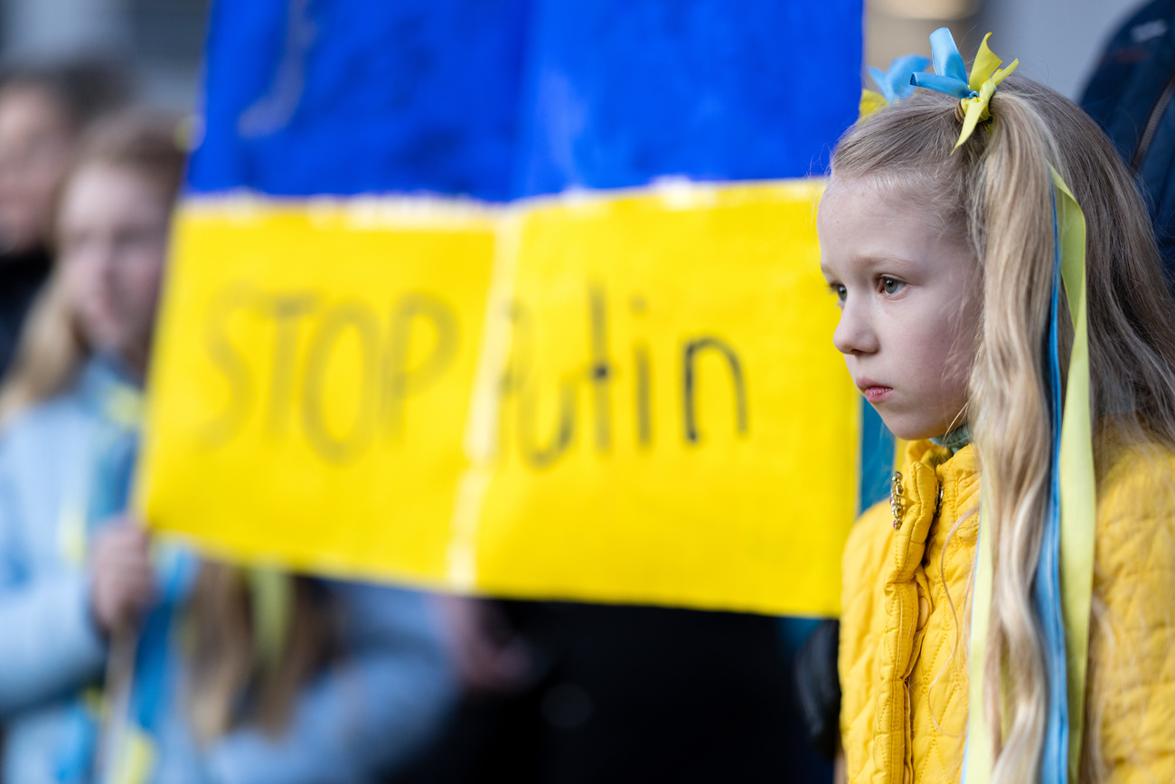 A child looks out with a Ukranian flag next to her, written are the words 'Stop Puti'.