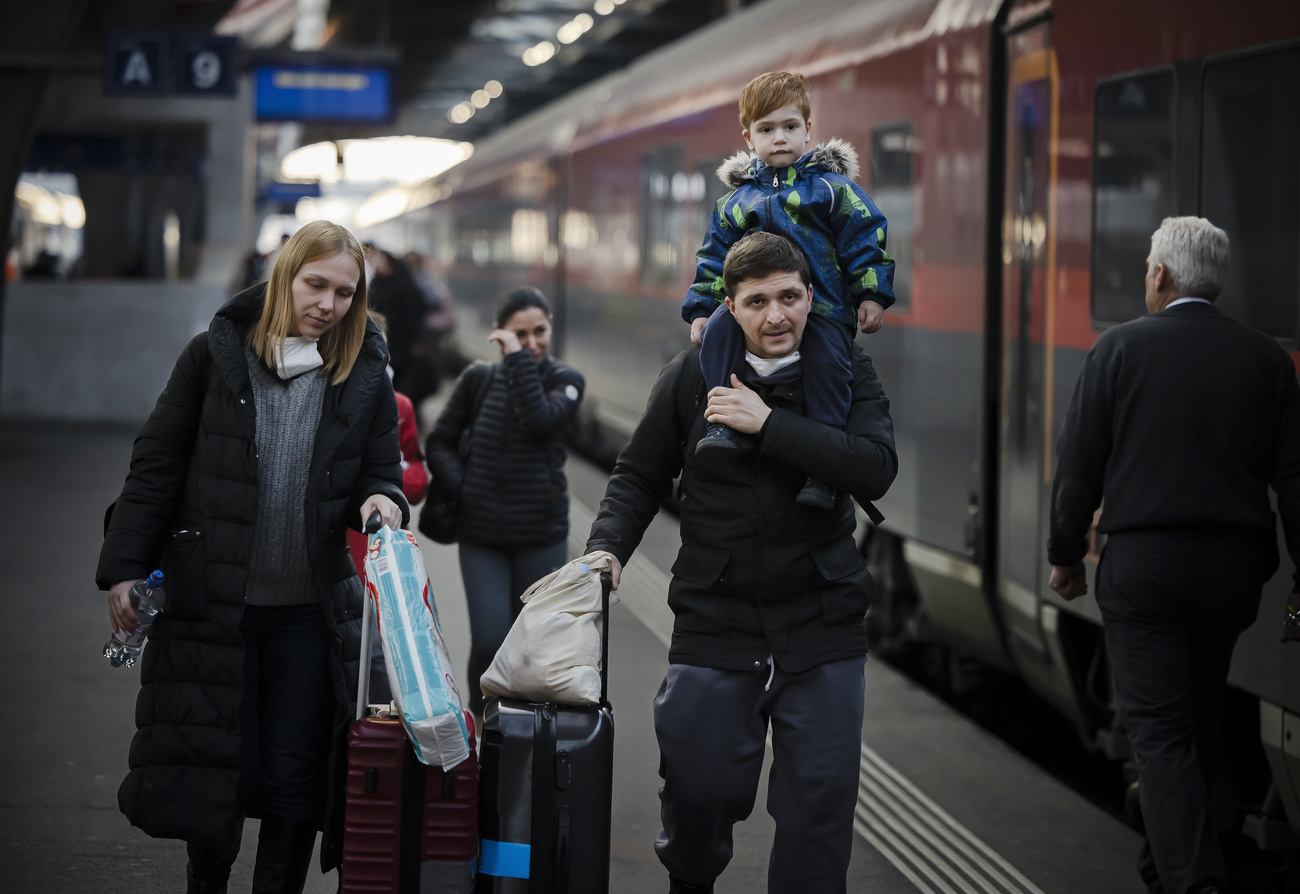 A family of two adults and two children push luggage along a train station platform.
