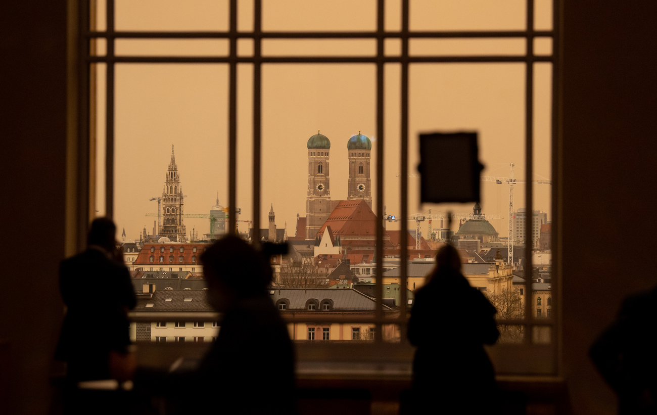 Мюнхен, Германия: журналисты стоят перед окном в здании парламента федеральной земли Бавария. Над центром города собирается облачный фронт, окрашивающей небо в желто-оранжевый цвет, причиной которого является пыль, принесенная из Сахары.