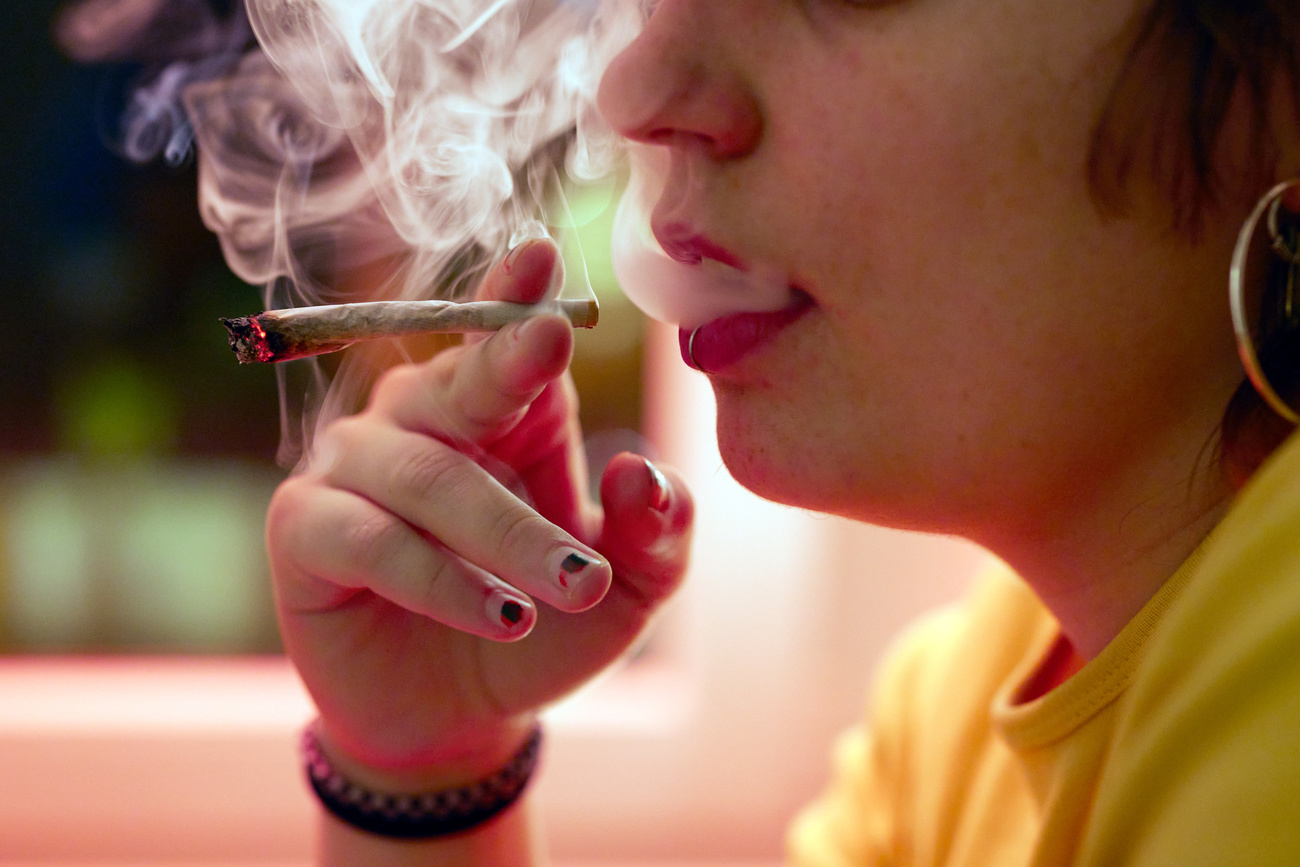 A young person with piercings, bracelets, and a yellow T-shirt smokes a joint