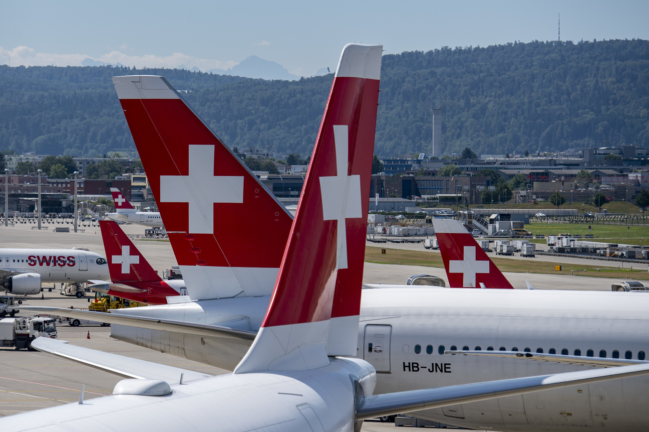 The tails of four SWISS airplanes line up on the runway at Zurich airport, showing the Swiss flag logo (a white plus on a red background)