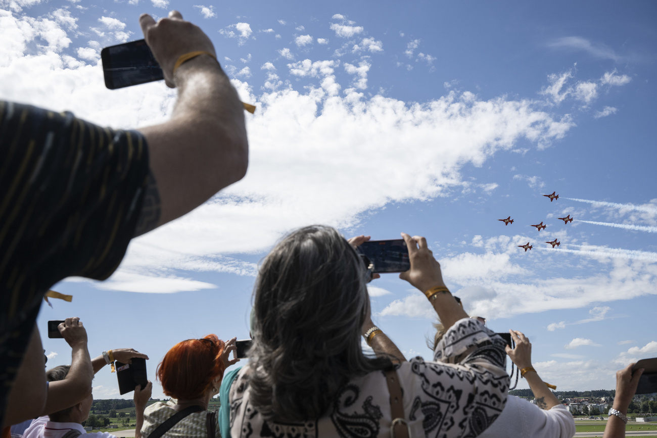 Fighter jets flying in formation are photographed by a crowd below.