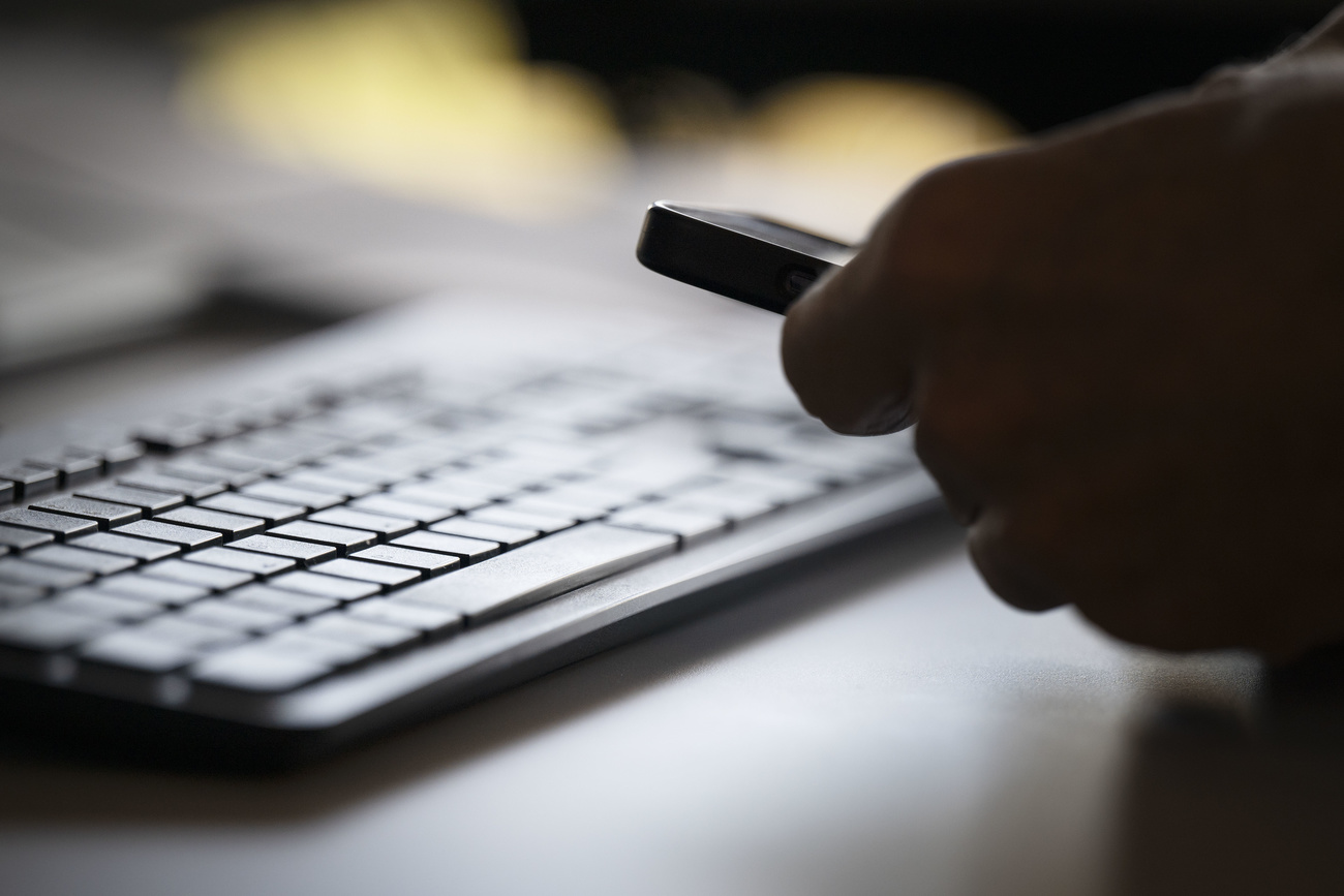 tastiera di computer e, in controluce, mano che tiene smartphone