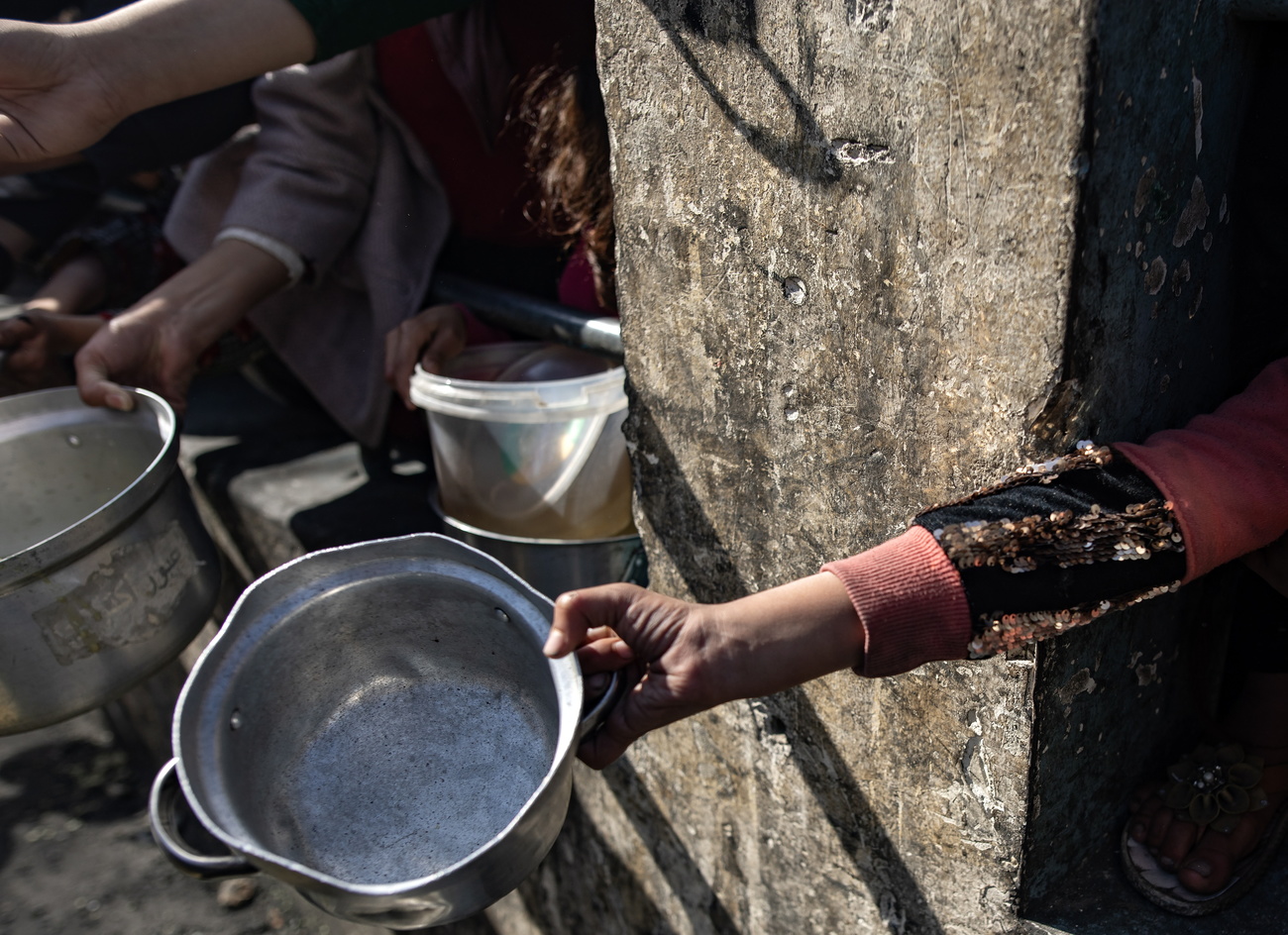 فلسطينيون وفلسطينيات نازحون.ات يحملون.ن أوانيًا ودلاء فارغة أثناء انتظارهم.نّ لتلقي المساعدات الغذائية التي تقدمها مجموعة شبابية فلسطينية في مخيم رفح للاجئين واللاجئات، جنوب قطاع غزة، 25 يناير 2024.