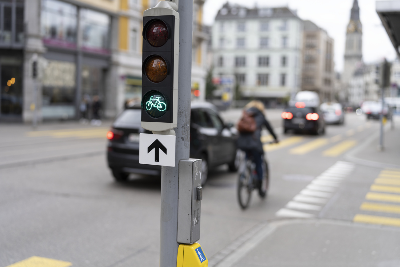 a commuter rides their bike in Zurich with a green light in the foreground. Cars drive alonside.