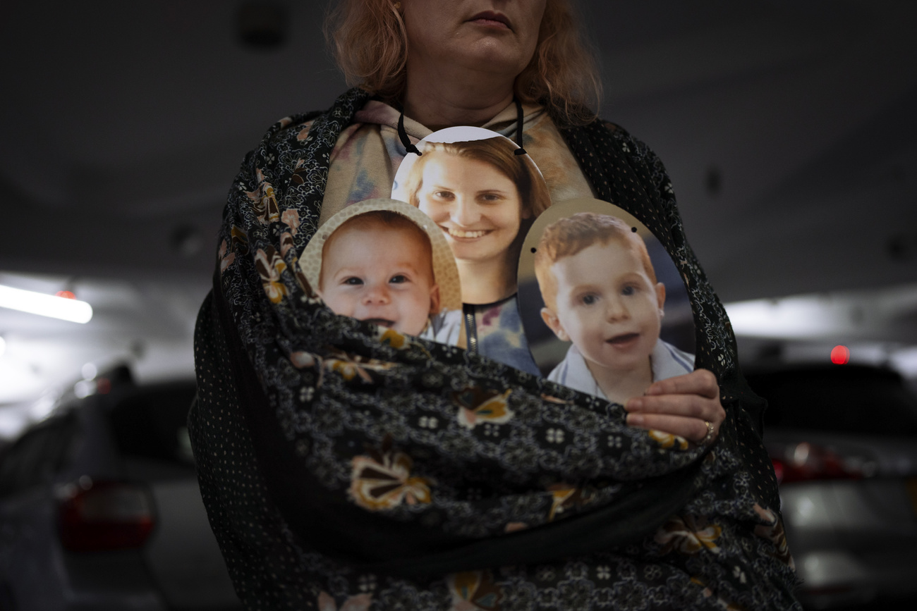 A woman holds a mask depicting the faces of children
