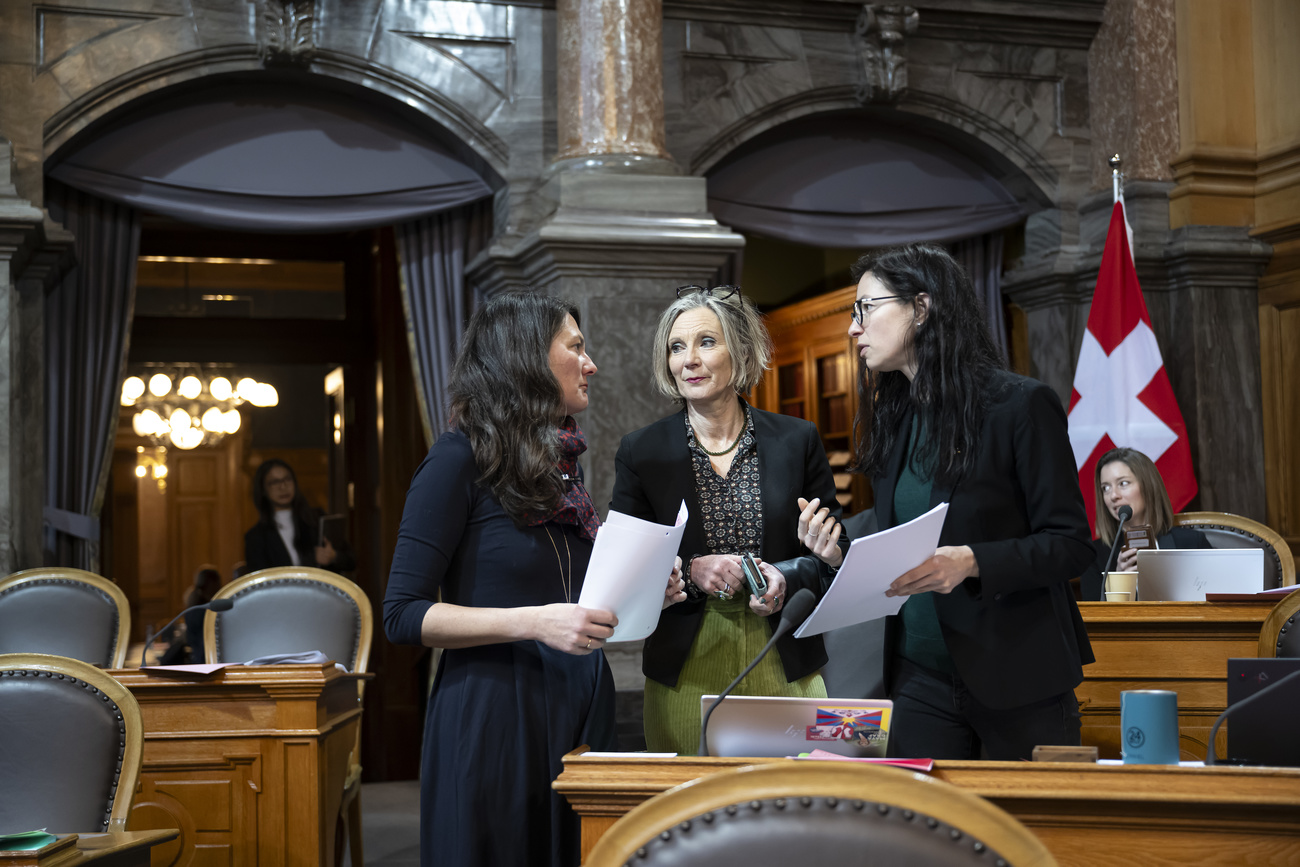 Trois femmes debout discutant dans la salle du Conseil des États.