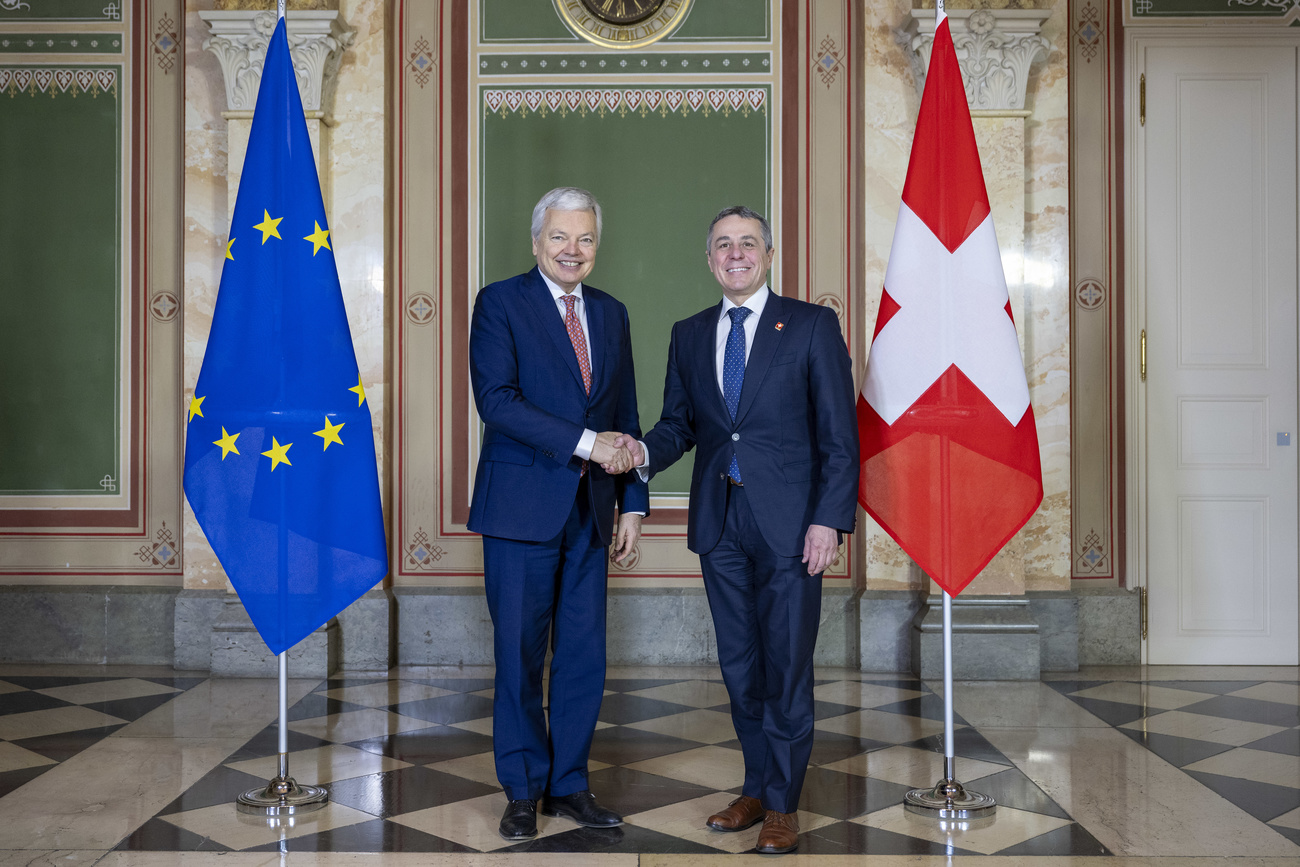 two men in blue suits with the EU flag on the left and the Swiss flag on the right