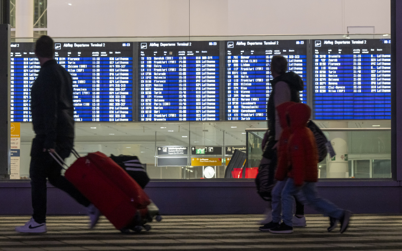 family with rolling suitcases walk past the large blue board of flight schedules