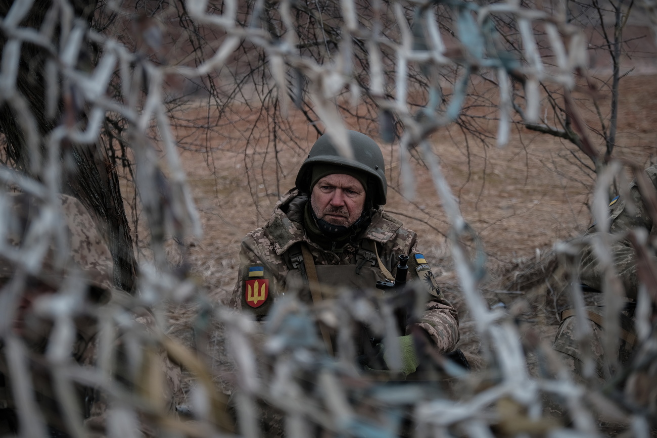 A Ukrainian soldier with helmet and uniform mans a position behind a camouflage net