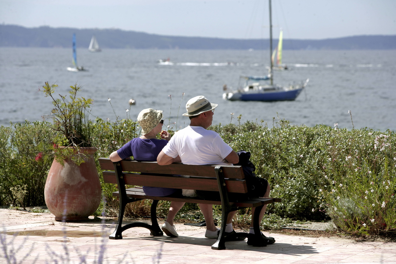 Due persone anziane su una panchina in riva al mare.