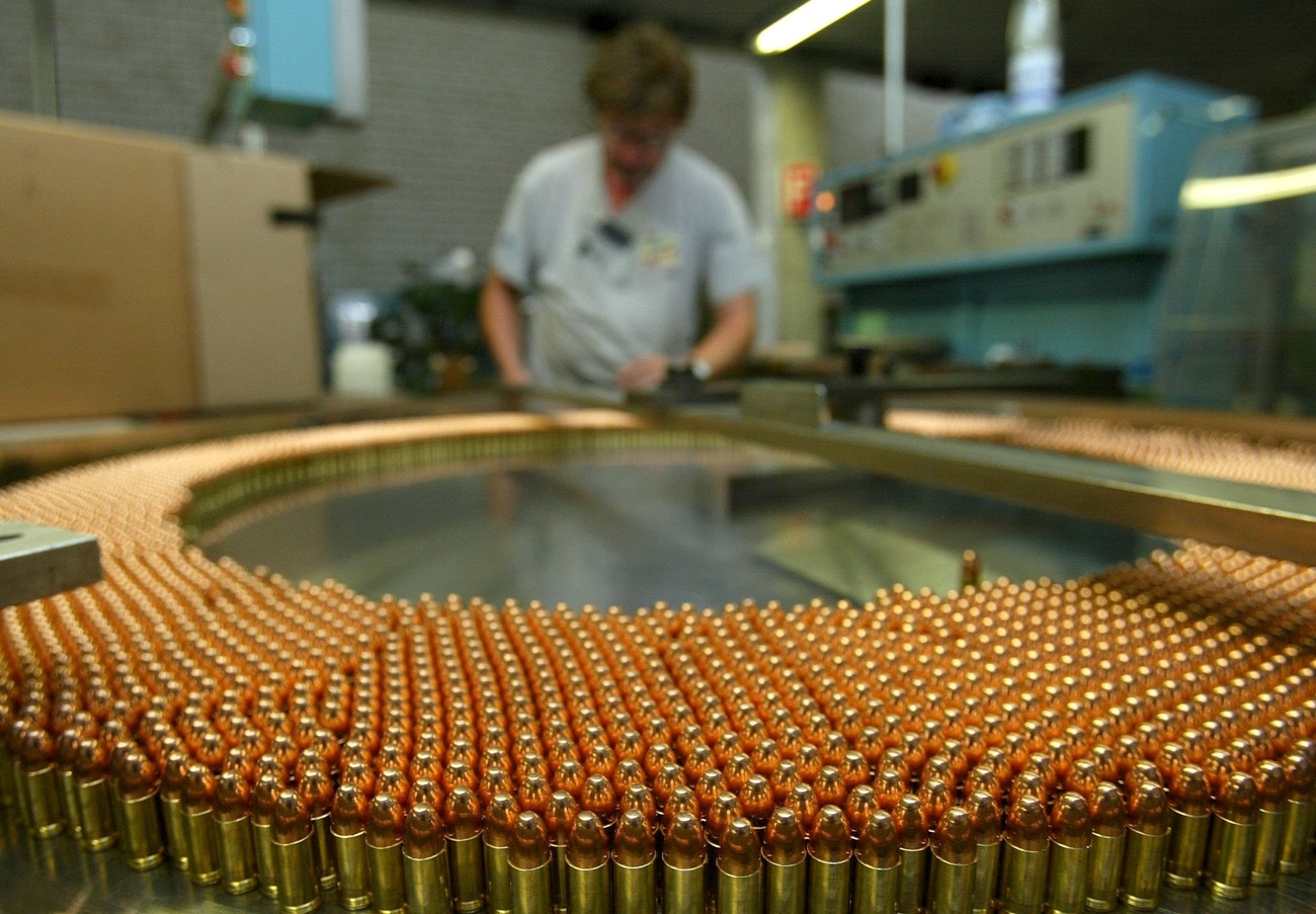 a man working in an ammunitions factory with rows of bronze coloured bullets.