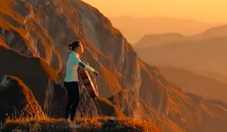 Junger Mann spielt Cello bei sonnenuntergang in den Bergen
