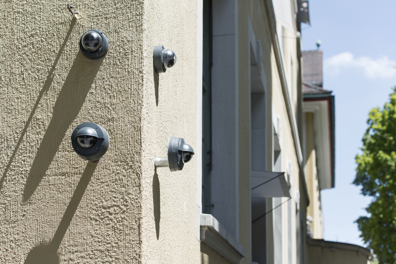 Four round black video cameras, two on either side of the corner of a building. They look like big round bolts, with a rounded, bulbous centre.