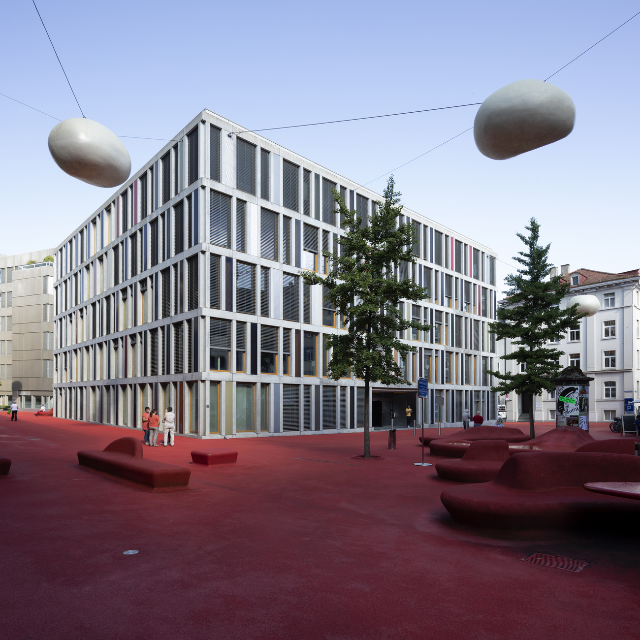 A large office building sits in front of a public square with red pavement.