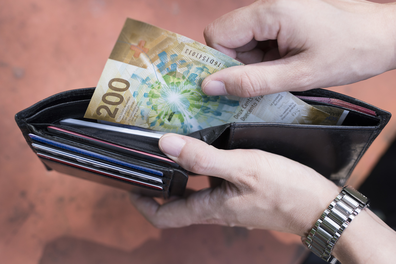 primo piano di mani che tolgono banconota da 200 franchi da un portafoglio