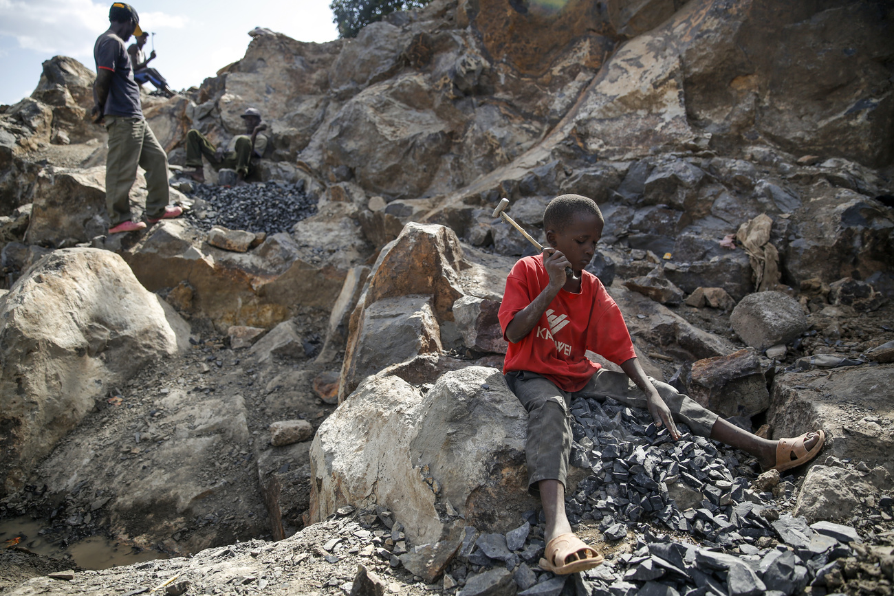 Ein Kind arbeitet in trostloser Umgebung in Kenia, es zertrümmert Steine mit einem Hammer.