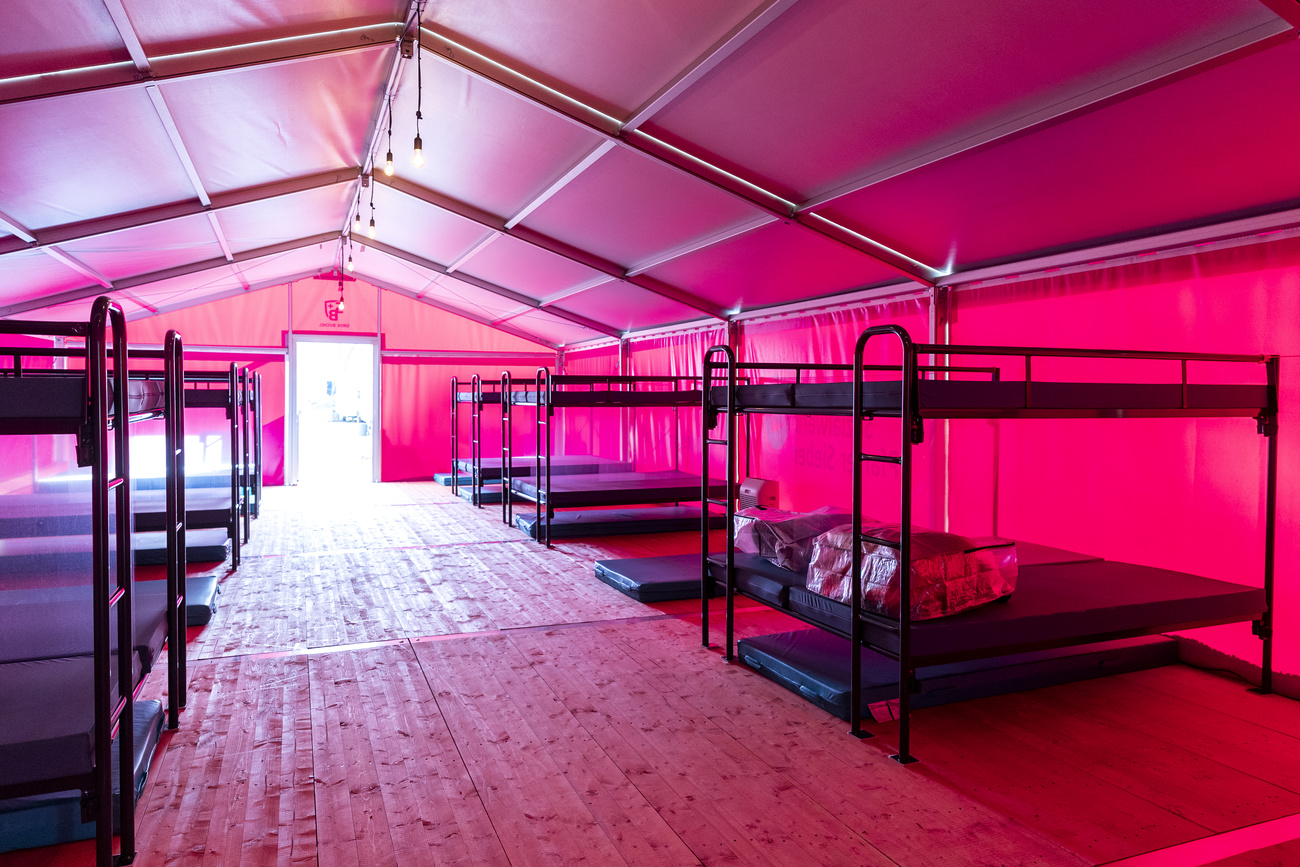 A large bright pink tent with wooden floors filled with metal bunk beds and blue plastic mattresses.
