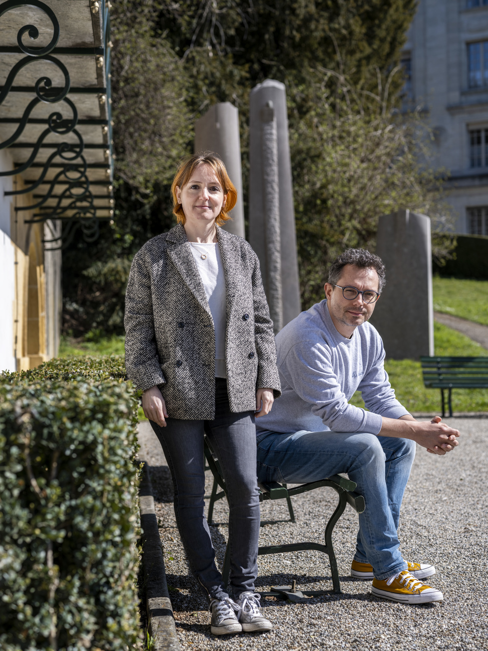 Femme debout et homme assis sur un banc dans un parc à Lausanne.