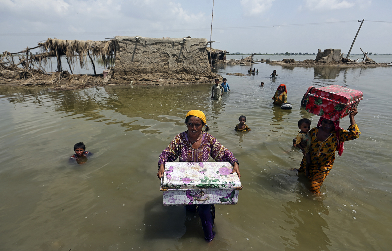 Floods in Pakistan force families to evacuate their homes. Women are holding boxes with their belongings as they walk in muddy waters.