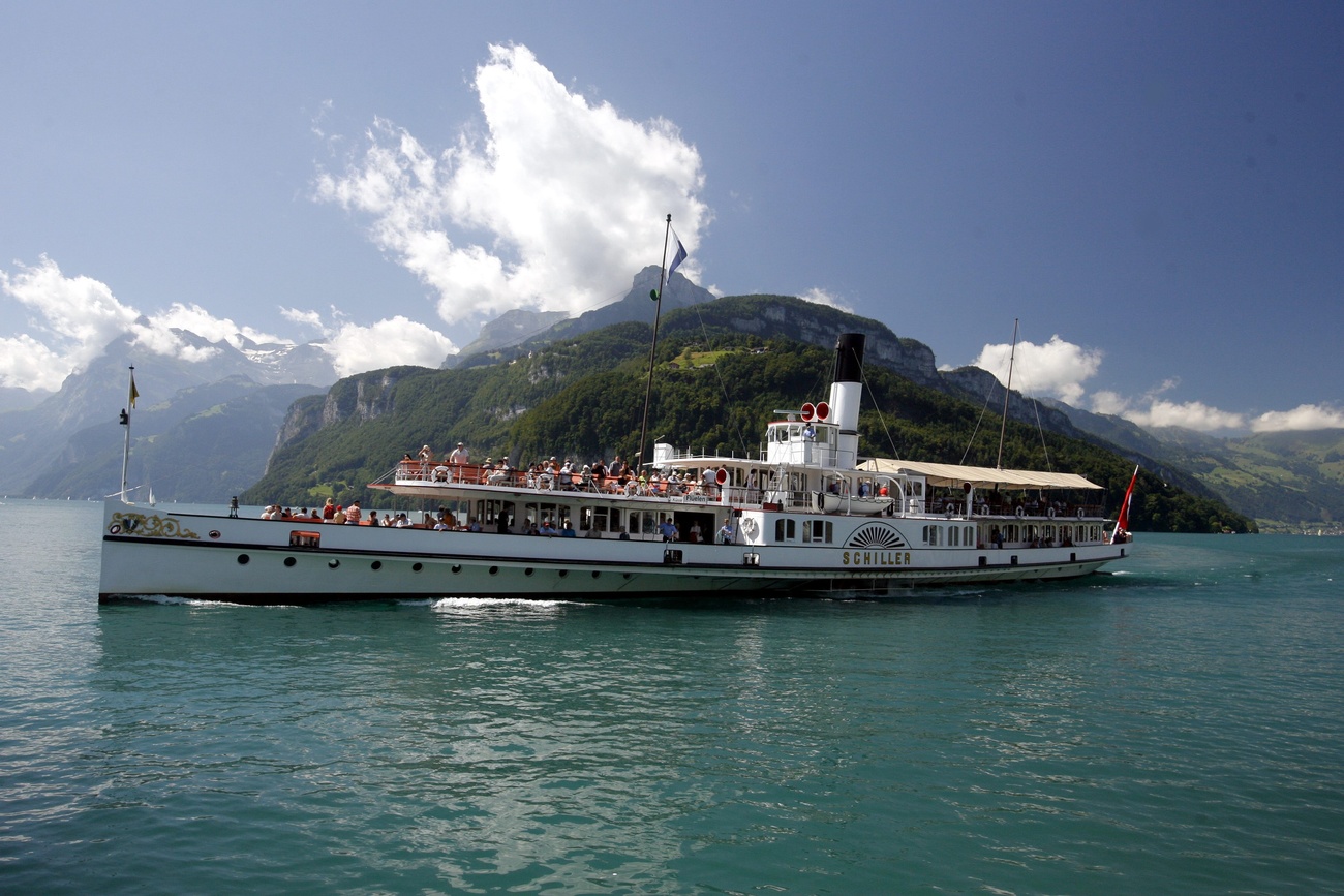 The white, 118-year-old steamboat Schiller sails on Lake Lucerne, with mountains in the background. It's a fairly sunny day with a light blue sky and a few clouds.