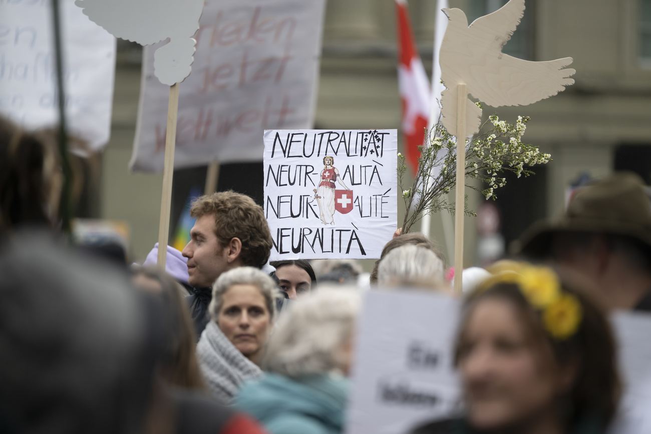 A neutrality protest in Switzerland. Cardboard dove cut-outs can be seen as well as white flowers and a placard saying ‘neutrality’ in multiple languages with the Swiss flag