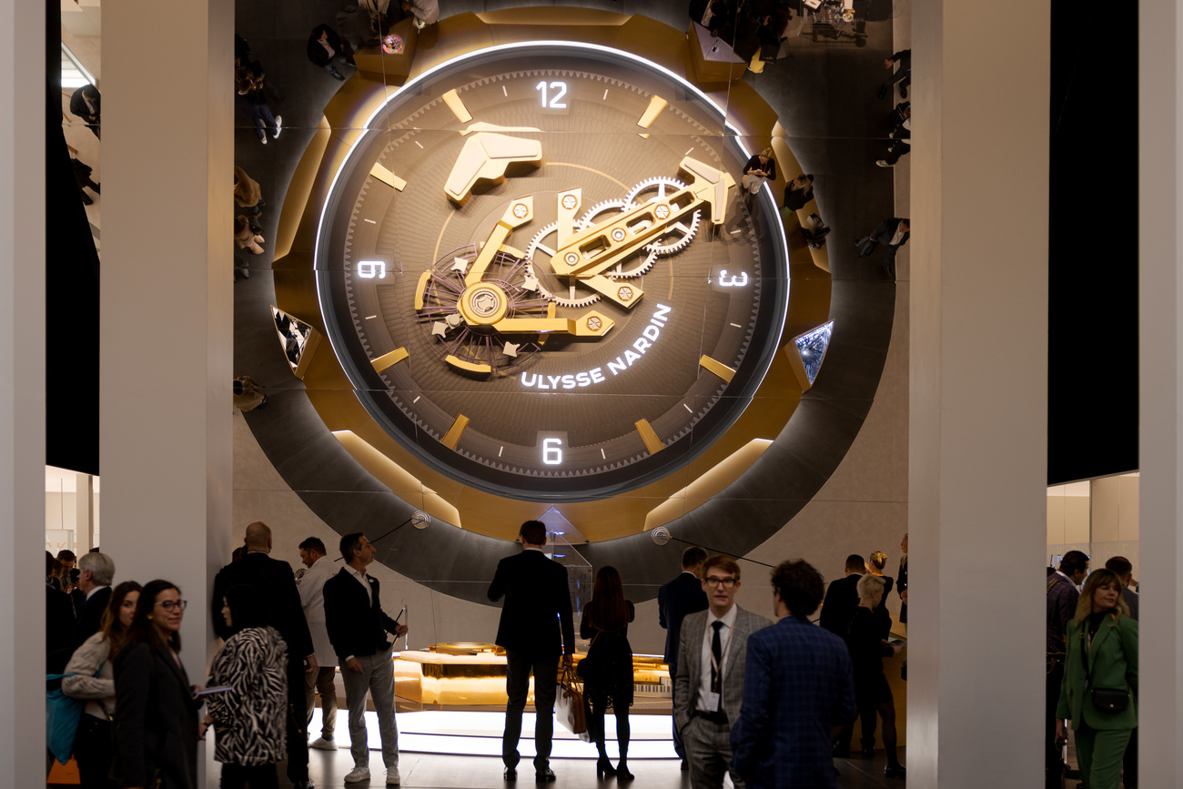 Groups of people mill around beneath a giant Ulysse Nardin watch face