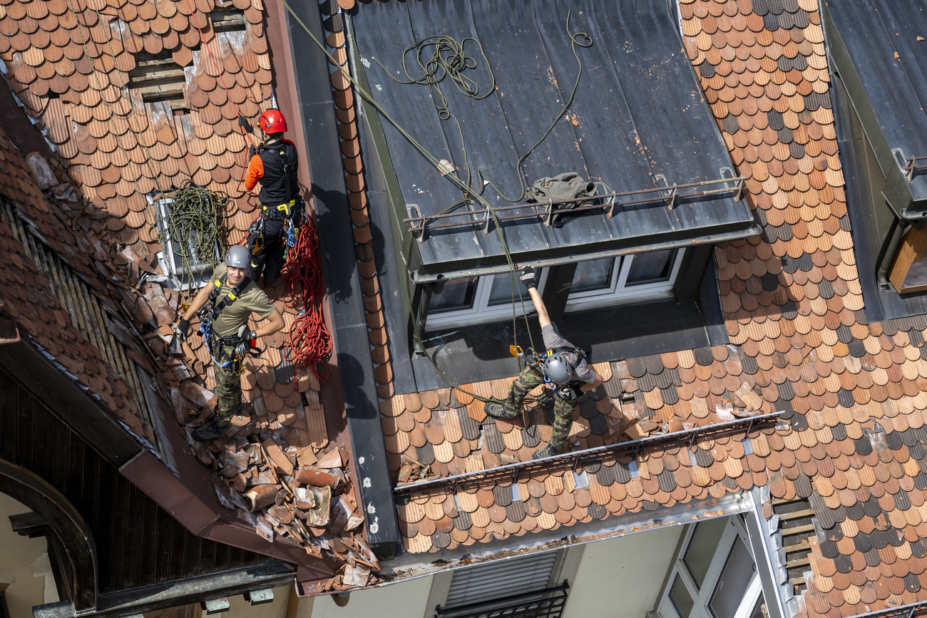 Swiss Army soldiers and firefighters remove roof tiles and secure a roof where damage is visible in the town of La Chaux-de-Fonds.