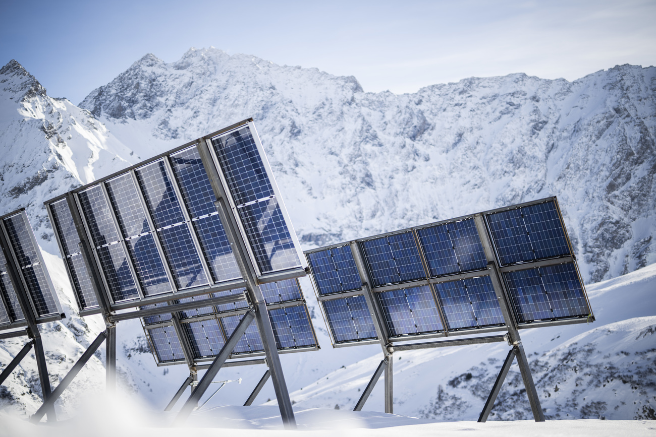 Solar panels are propped up on a bright, sunny day, facing a snowy mountain range