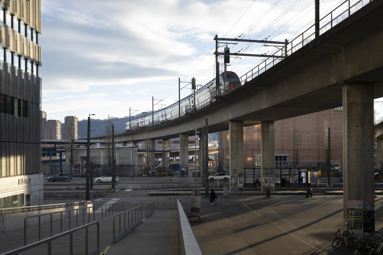 A double-decker train passes over a bridge, above a main road in the city of Zurich