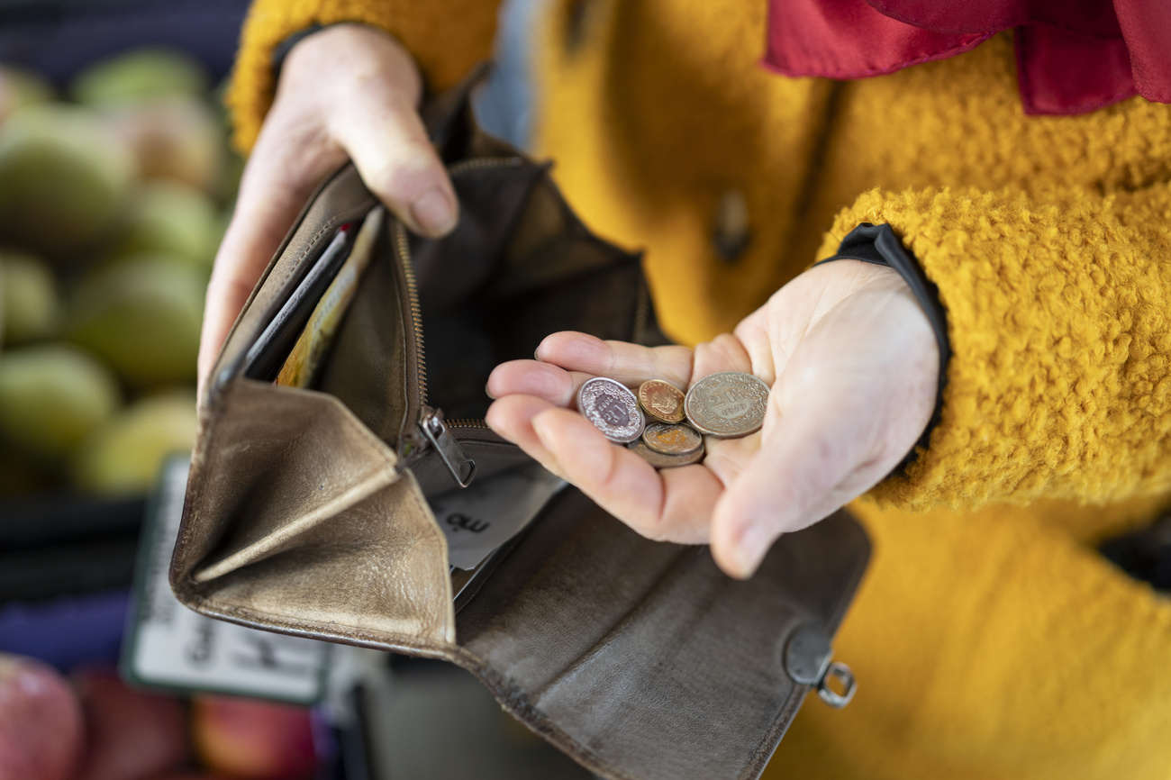A woman’s hand and the sleeve of a bright yellow fluffy coat are visible taking several Swiss coins out of a brown wallet. The coins are in her palm.