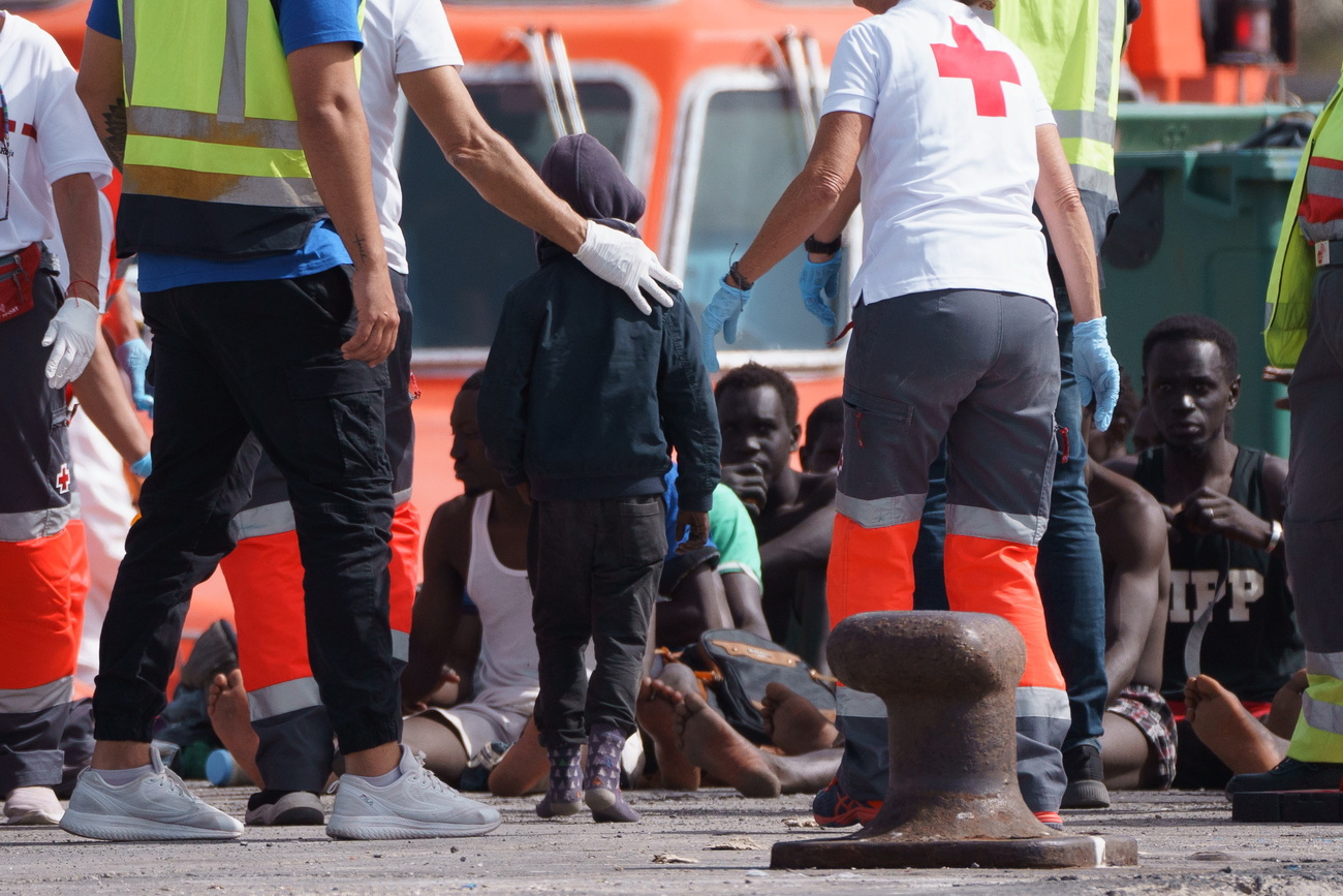migranti seduti a terra vengono accolti da personale sanitario
