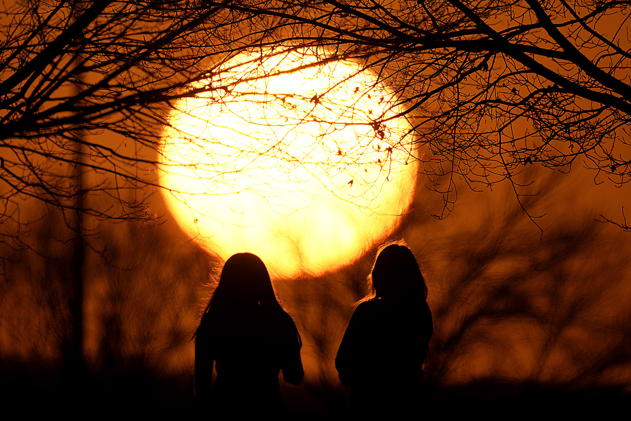 Due persone osservano il grande disco solare al tramonto.